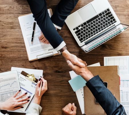 Birdseye view of two people shaking hands above paperwork and laptops on a table